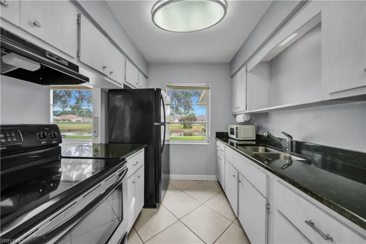Kitchen featuring electric range oven, extractor fan, white cabinets, and dark stone countertops