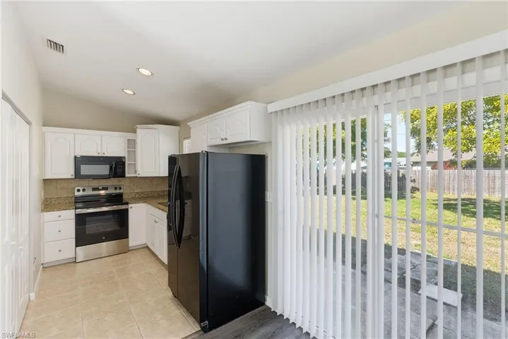 Kitchen with black appliances, vaulted ceiling, healthy amount of natural light, white cabinetry, and decorative backsplash