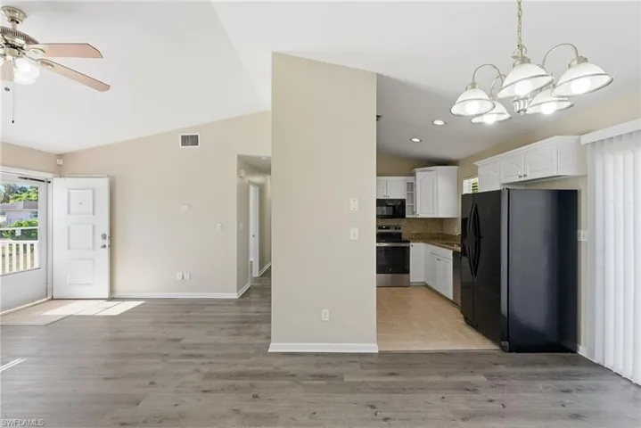 Kitchen with black appliances, white cabinetry, healthy amount of natural light, vaulted ceiling, and hanging light fixtures