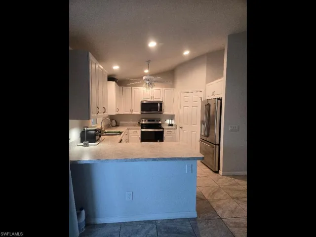 Kitchen with light countertops, stainless steel appliances, white cabinetry, a peninsula, and ceiling fan