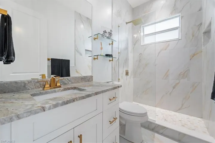 Bathroom with a marble finish shower, toilet, marble finish floor, and vanity
