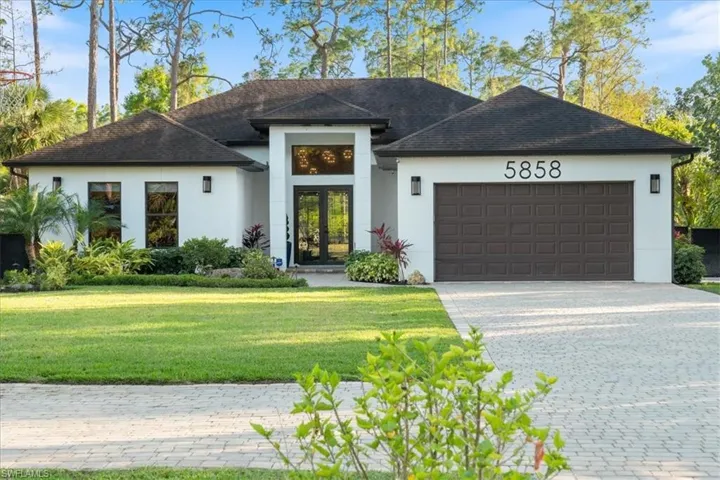 View of front facade with stucco siding, french doors, decorative driveway, an attached garage, and a front lawn