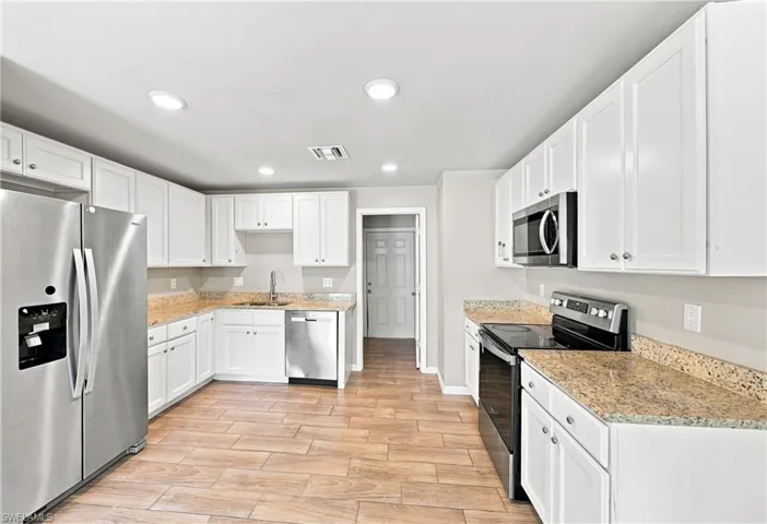 Kitchen featuring white shaker cabinetry, stainless steel appliances, speckled stone countertops, and wood-finish tile flooring