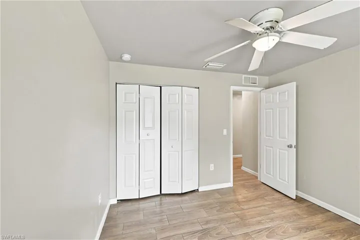 Wood-finish flooring, neutral painted walls, ceiling fan with integrated lighting, white bi-fold closet doors, and a white paneled interior door