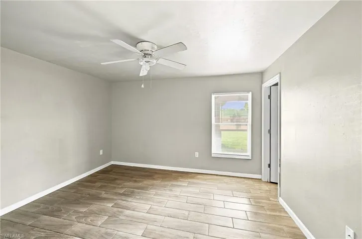 Wood-finish tile flooring throughout, featuring a ceiling fan, window with white trim, and a white interior door