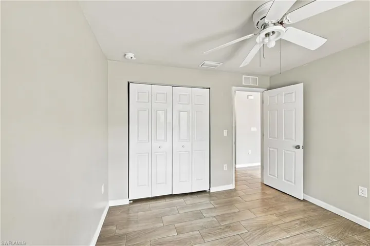 Neutral wall color, wood-finish tile flooring, bifold closet doors, ceiling fan with integrated lighting, and a six-panel door