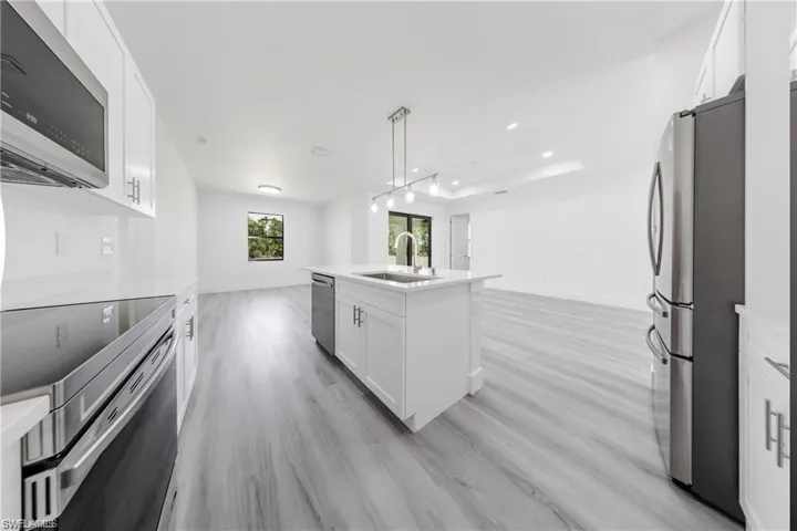 Kitchen with stainless steel appliances, white cabinetry, open floor plan, hanging light fixtures, and a raised ceiling