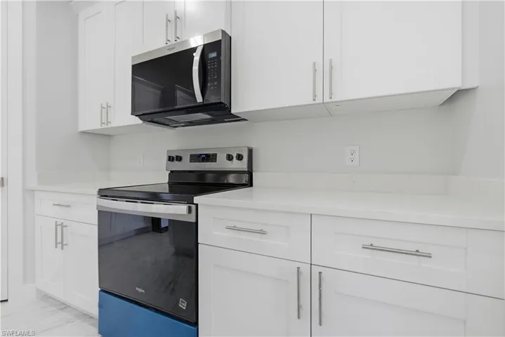 Kitchen with stainless steel appliances, white cabinetry, light marble finish flooring, and light stone counters