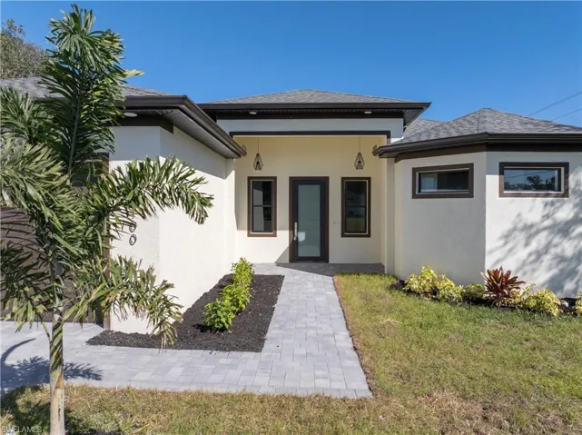 Entrance to property with stucco siding, a yard, roof with shingles, and covered porch