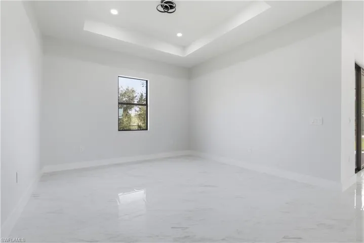 Empty room featuring light marble finish flooring, a raised ceiling, and recessed lighting