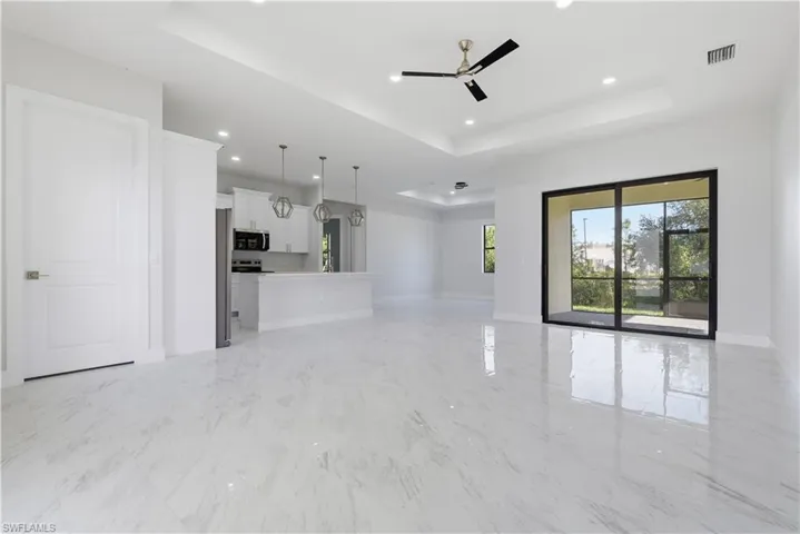Unfurnished living room featuring a tray ceiling, light marble finish flooring, a ceiling fan, and recessed lighting