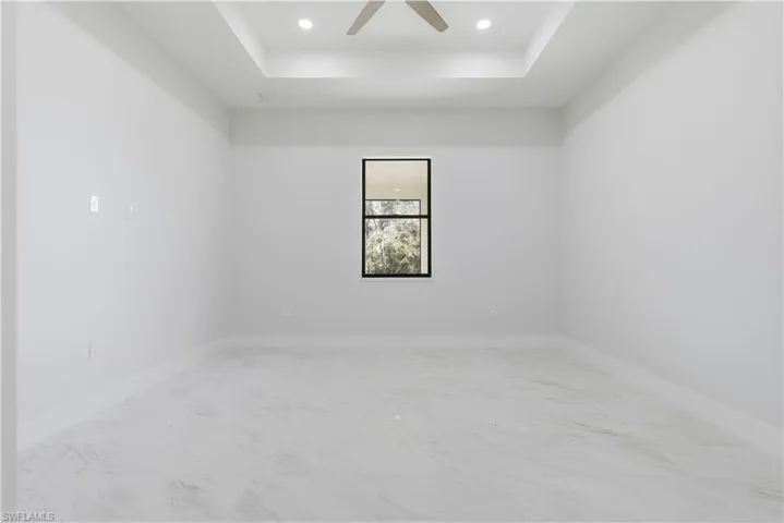 Spare room with a tray ceiling, ceiling fan, recessed lighting, and light marble finish flooring