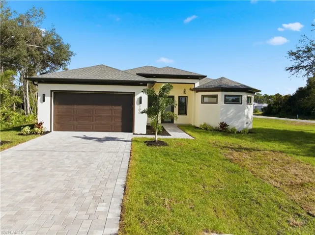 Prairie-style home with stucco siding, decorative driveway, a front lawn, and an attached garage
