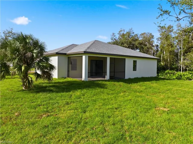 Back of property with a yard, stucco siding, a sunroom, and roof with shingles