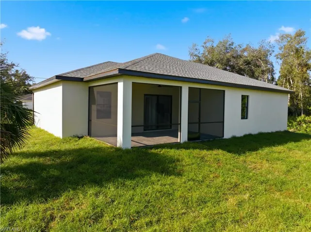 Back of property with stucco siding, a yard, ceiling fan, and roof with shingles