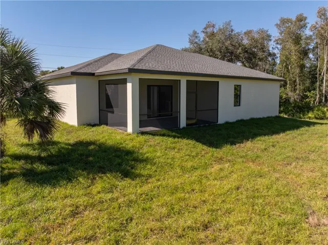 Rear view of house featuring a yard, stucco siding, roof with shingles, and a sunroom