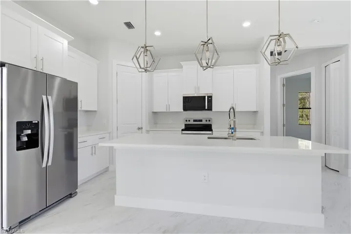Kitchen with appliances with stainless steel finishes, white cabinetry, an island with sink, decorative light fixtures, and recessed lighting