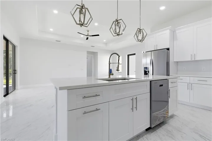 Kitchen featuring white cabinetry, stainless steel appliances, light marble finish flooring, a kitchen island with sink, and a raised ceiling