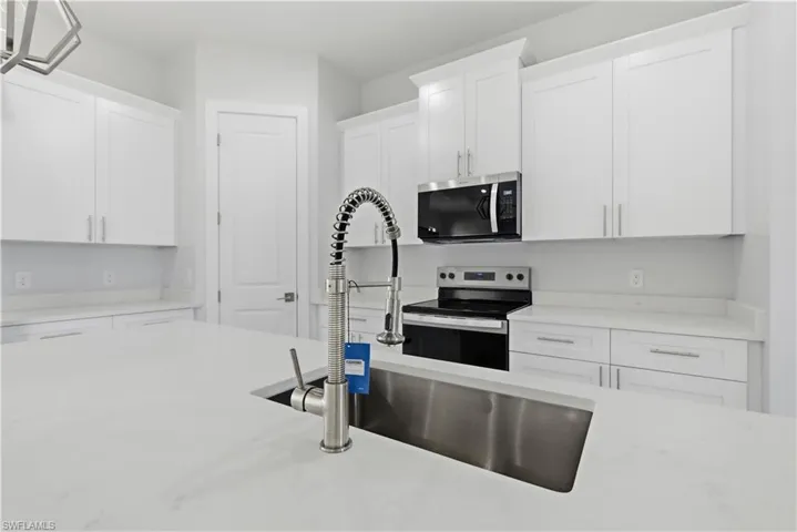 Kitchen with stainless steel appliances, white cabinetry, and light stone countertops