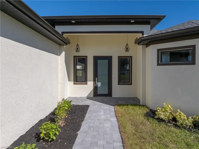 Property entrance featuring stucco siding, covered porch, and a lawn
