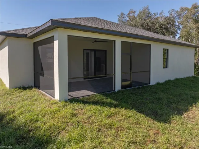 Back of house featuring a lawn, stucco siding, roof with shingles, and a sunroom