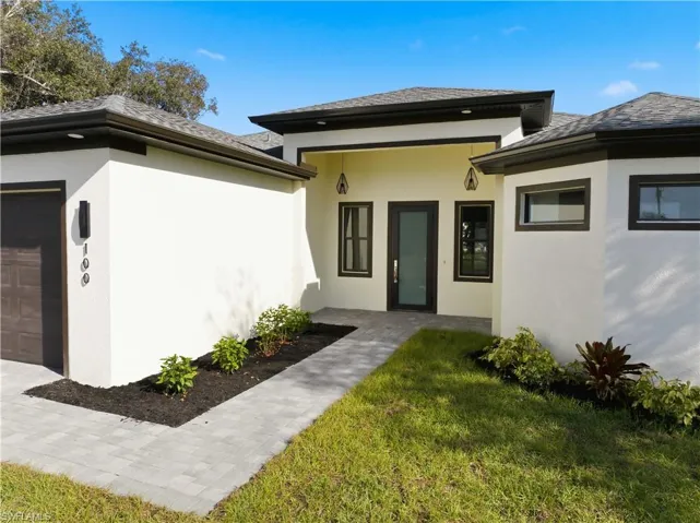 Doorway to property with stucco siding, a lawn, and a garage