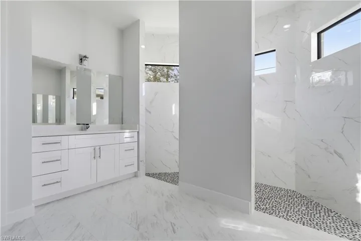Bathroom with plenty of natural light, vanity, a marble finish shower, and light marble finish floors
