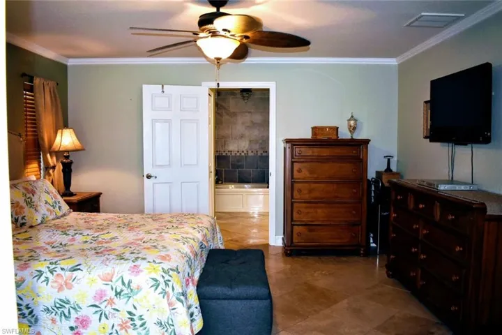 Tiled bedroom with crown molding, ceiling fan, and connected bathroom
