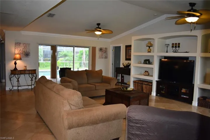 Living area with built in shelves, ceiling fan, crown molding, vaulted ceiling, and light tile patterned floors