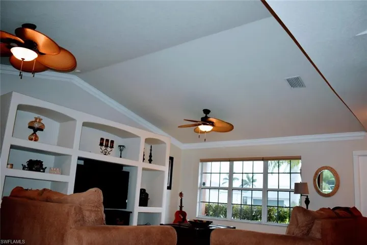 Living area with a ceiling fan, crown molding, built in shelves, and vaulted ceiling