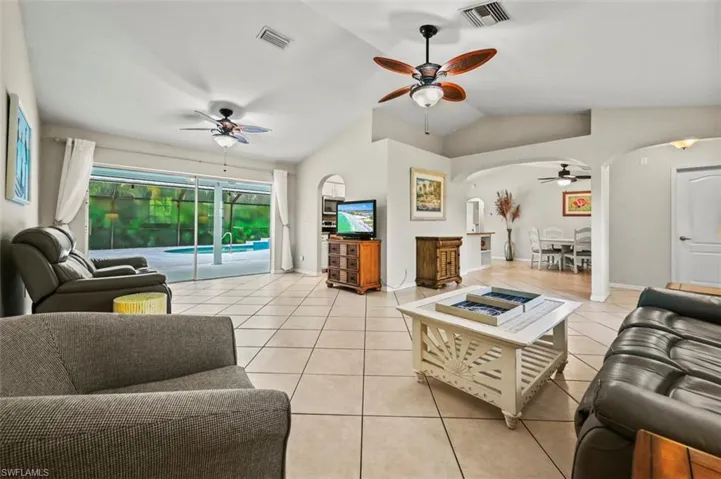 Living room featuring ceiling fan, arched walkways, lofted ceiling, and light tile patterned floors