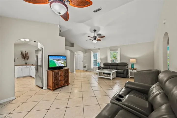 Living area with a ceiling fan, arched walkways, lofted ceiling, and light tile patterned floors