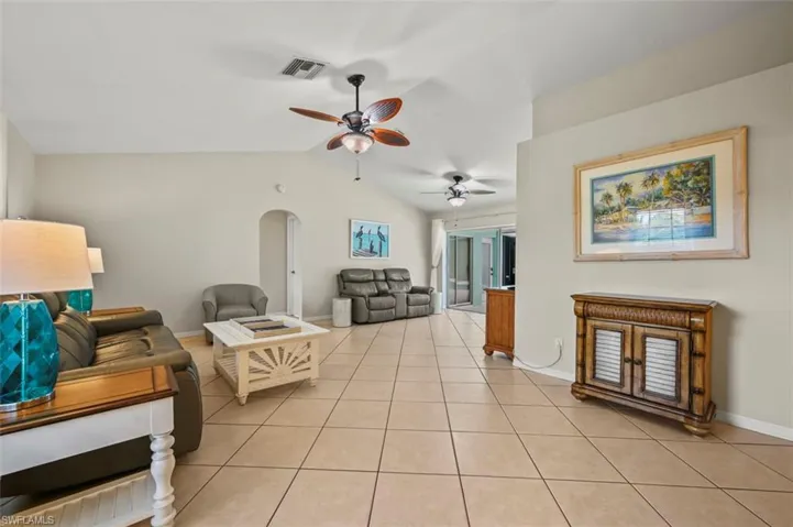 Living area featuring lofted ceiling, light tile patterned floors, a ceiling fan, and arched walkways