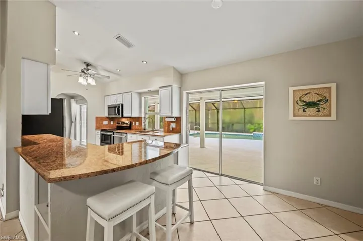 Kitchen with a peninsula, stainless steel appliances, light tile patterned floors, a breakfast bar, and light stone countertops