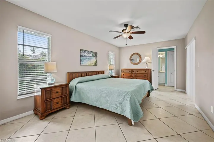 Bedroom featuring light tile patterned floors, ensuite bathroom, and ceiling fan