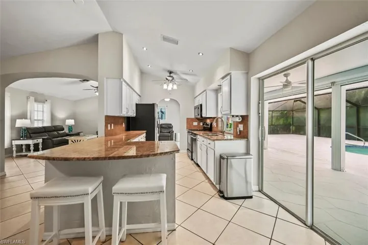 Kitchen with arched walkways, ceiling fan, a kitchen breakfast bar, dark stone countertops, and recessed lighting