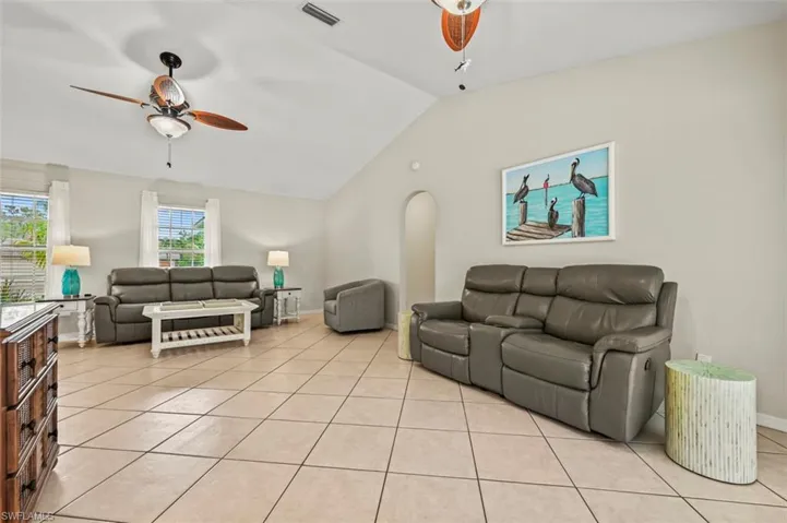 Living room featuring a ceiling fan, lofted ceiling, and light tile patterned floors