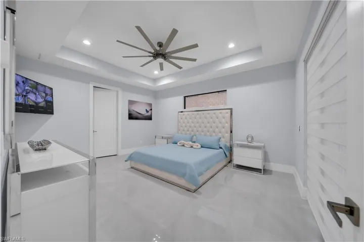 Spacious room featuring glossy tile flooring, a tray ceiling with recessed lighting, and a modern ceiling fan