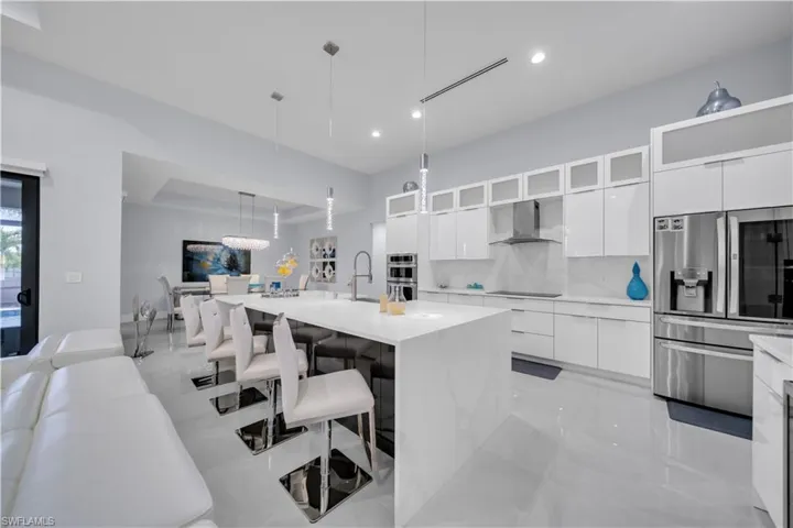 Modern kitchen featuring a large waterfall island, white cabinetry, integrated stainless steel appliances, and sleek tile flooring