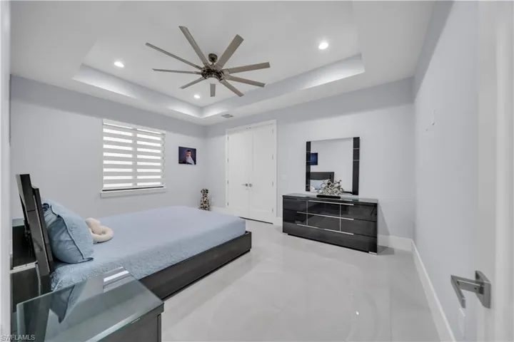 Recessed lighting illuminating a spacious room with a tray ceiling and a multi-blade ceiling fan