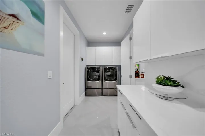 Dedicated laundry area featuring a full-size washer and dryer, extensive white cabinetry, a bright countertop, modern recessed lighting, and large format floor tile
