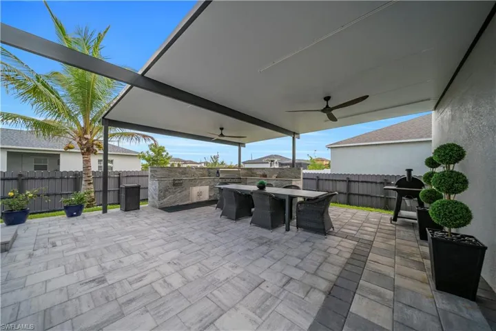 Behind RV Garage Expansive covered patio featuring a stone-look paver surface, integrated outdoor kitchen with stone veneer, and dual ceiling fans