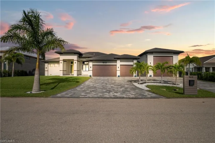 Contemporary exterior featuring a paver driveway, multiple garage doors, and a tropical landscape with palm trees and manicured lawn