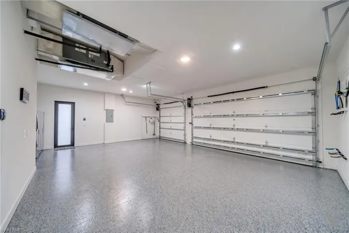 Spacious garage featuring a speckled epoxy floor, two overhead garage doors, recessed lighting, and a frosted glass-paneled entry door