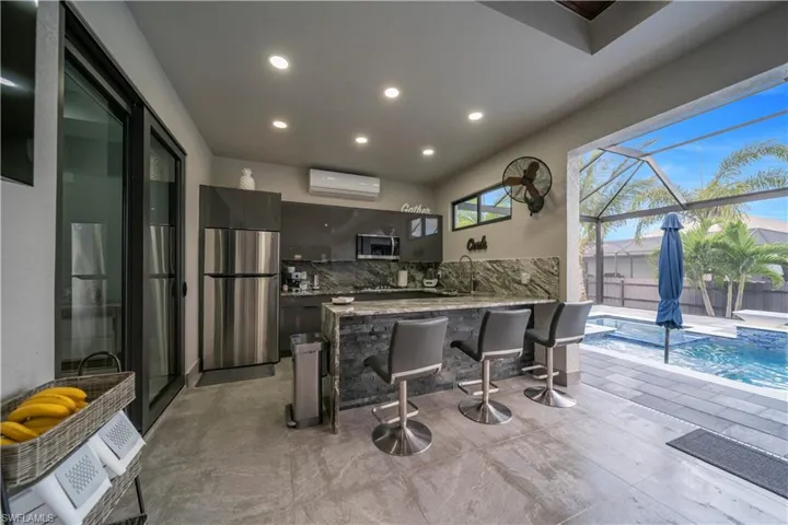 Outdoor kitchen featuring stainless steel appliances, stone slab countertops, and a stone-clad island with built-in seating