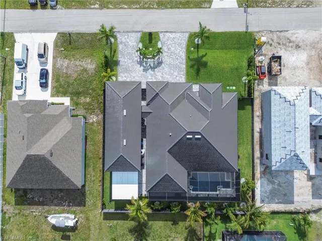 Modern rooflines characterize this property, featuring a screened-in pool area, a paved driveway, and mature palm trees