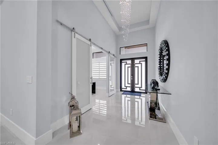 Grand entryway featuring a double-door entrance with geometric detailing, high ceilings with a crystal chandelier, and large format tile flooring