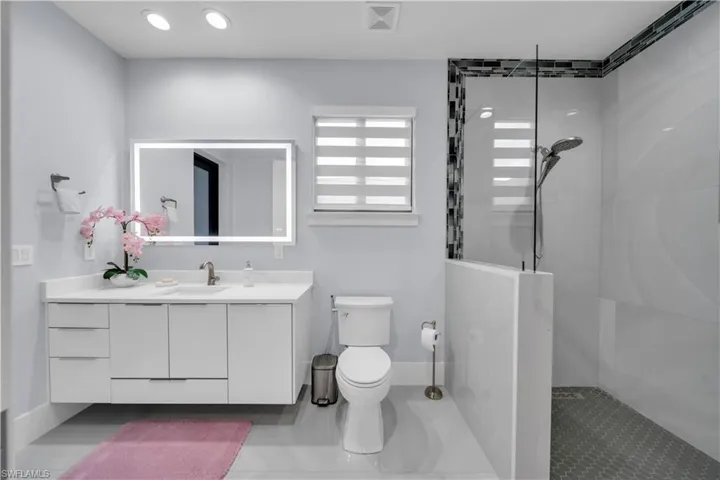 Contemporary bathroom featuring a floating white vanity with integrated sink, illuminated mirror, and a walk-in shower with glass partition and mosaic accent tile