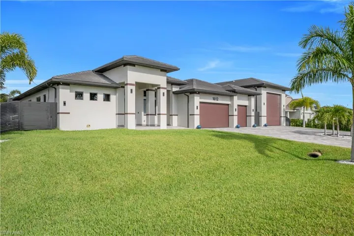 Modern stucco exterior featuring a flat tile roof, three brown garage doors, a paver driveway, and a spacious front lawn