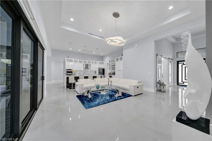Spacious open-concept living area featuring large format light-toned tile flooring, recessed lighting, and a contemporary chandelier